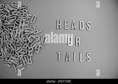 HEADS OR TAILS in wooden English language capital letters spilling from a pile of letters in black and white Stock Photo