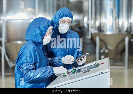 Side view portrait of two workers using control panel while operating equipment at factory Stock Photo