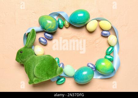 Frame made of Easter eggs, candies, ribbon and bunny on color background Stock Photo