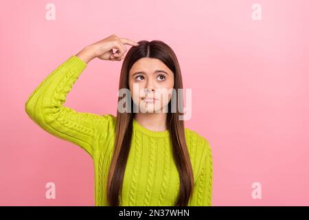 Photo portrait of pretty young schoolgirl scratching head look empty space dressed stylish green outfit isolated on pink color background Stock Photo