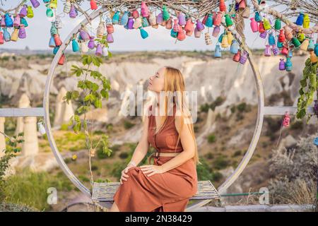 Young woman exploring valley with rock formations and fairy caves near Goreme in Cappadocia Turkey. Wish tree. Small multi-colored jugs with Stock Photo