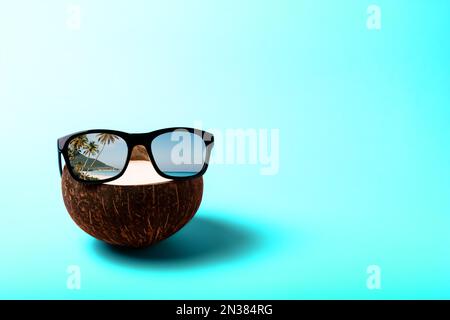 Summer composition on the theme of vacation. Funny coconut with sunglasses on a blue background, the color of the sea or ocean. Reflection of palm tre Stock Photo