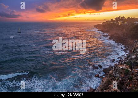 Red colorful sunset and vivid dramatic sky at rocky shore of the Atlantic ocean. Stock Photo
