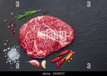 Raw ribeye steak on stone black serving plate. Flat lay. Stock Photo