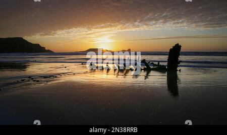 Sunset over the shipwreck of the Helvetia on Rhossili bay in front of Worms Head on the Gower peninsula in Swansea UK Stock Photo