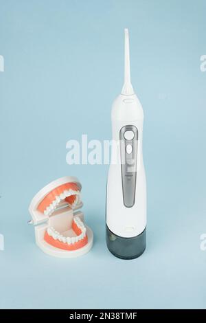 Dental Teeth Model dentures with oral cavity irrigator that cleans teeth on blue background, close-up. Stock Photo