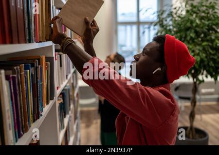 Concentrated African American student man picking books for preparing for exam in university library Stock Photo