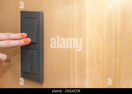 Turn on the light, a woman's hand presses the switch in the apartment close-up. Black light switch on the background of a wooden wall. The concept of Stock Photo