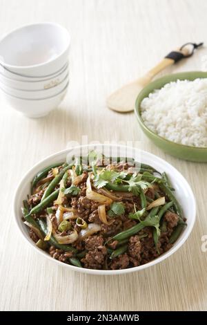 Ground beef stir fry with green beans and onions in white bowl with side dish of rice Stock Photo
