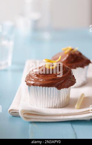 Chocolate frosted cupcakes with lemon zest and a candle on a blue background Stock Photo