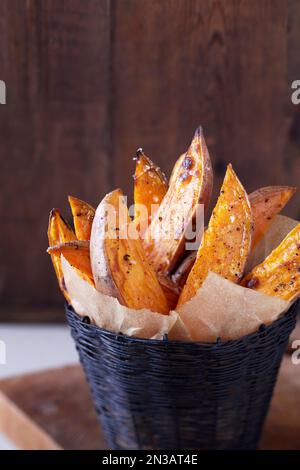 Roasted sweet potato wedges with sea salt and pepper in a black basket with parchment paper Stock Photo