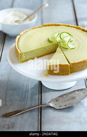 Avocado cheesecake topped with limes on a cake stand with a slice cut out Stock Photo
