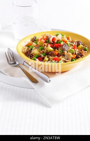 Fried Rice with pieces of beef, peppers, peas, celery, mushrooms and onion in a yellow bowl Stock Photo