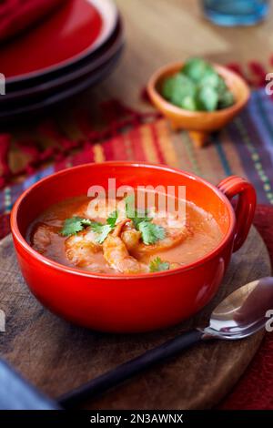 Tomato and shrimp soup in a red bowl topped with cilantro Stock Photo