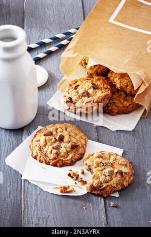 Milk bottle and oatmeal chocolate chip cookies in a brown paper bag and a cookie with a bite taken out of it with crumbs Stock Photo