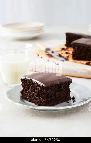 Piece of dark, chocolate cake with chocolate icing on a dessert plate with a glass of milk Stock Photo