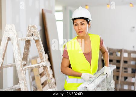 Woman builder carrying stepladder Stock Photo