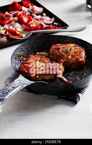 Glazed pork chops in a cast iron skillet with roasted vegetables in the background Stock Photo