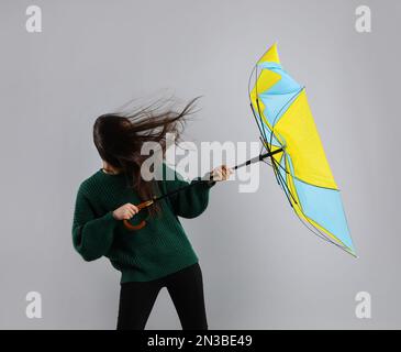 Woman with umbrella caught in gust of wind on grey background Stock Photo