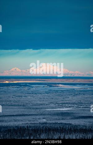 Mt Denali shines in the sun beneath the clouds above the frosty winter trees and Anchorage Alaska with the Joint Base Elmendorf Richardson Military... Stock Photo