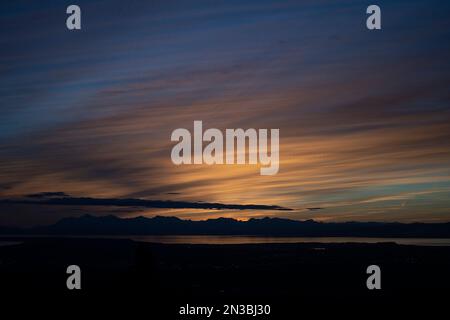 The sun sets above the Tordrillo Mountains across Cook Inlet from Anchorage, Alaska, on Dena’ina land, with the Knik arm in view Stock Photo