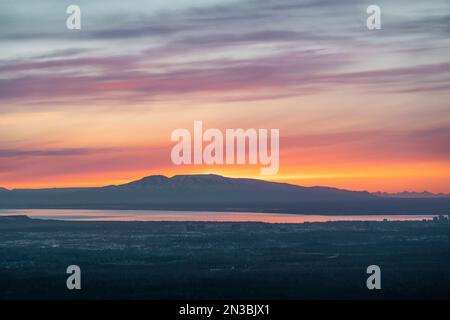 The sun sets above Mt. Susitna, or Sleeping Lady, across Cook Inlet from downtown Anchorage, Alaska on Dena’ina land, with Knik arm in view Stock Photo