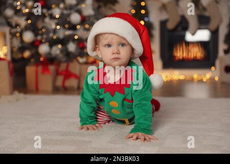Cute baby wearing Santa's elf clothes in room with Christmas decorations Stock Photo