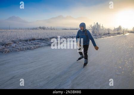 A caucasian man backcountry ice skating, nordic blading, away from the winter sun on a partly sunny, partly foggy, winter day with frost covered gr... Stock Photo