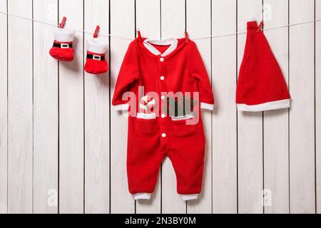 Cute Christmas baby clothes hanging on white wooden wall Stock Photo