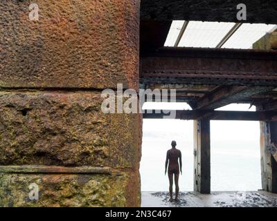 View taken from behind of Antony Gormley's Another Time 1999-2013, cast iron figure, Folkestone Harbour Arm; Folkestone, Kent, England, United Kingdom Stock Photo