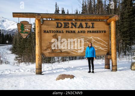 Portrait of a woman tourist standing in front of the sign at the main entrance of Denali National Park And Preserve Stock Photo