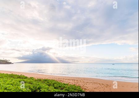 Sun beams shining through the clouds over the Island of Lanai with the pale turquoise water of the Pacific Ocean lapping the sandy shore of Kaanapa... Stock Photo
