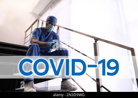 Tired overwhelmed doctor sitting on stairs in hospital. Medical system collapse during coronavirus pandemic Stock Photo