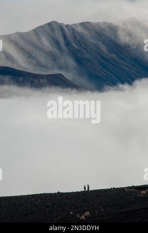 Hikers silhouetted by early morning clouds drifting through Haleakala National State Park on the southwest side of the island of Maui Stock Photo