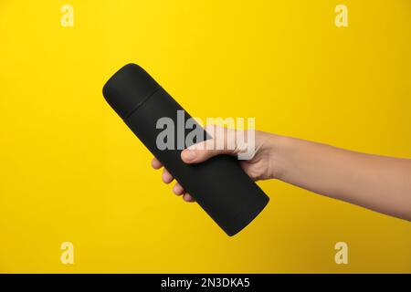 Woman holding modern black thermos on yellow background, closeup Stock Photo
