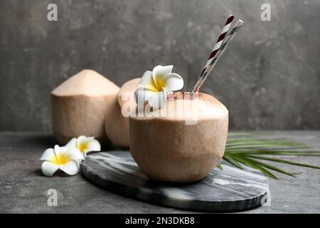 Young peeled coconuts with straw, palm leaf and beautiful flowers on grey table Stock Photo