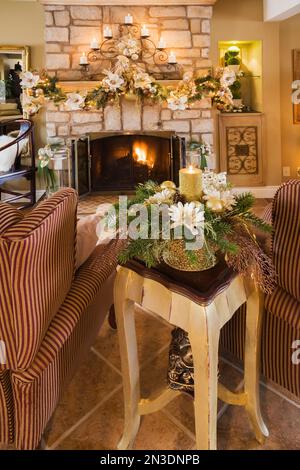 Two upholstered armchairs in front of natural cut stone wood burning fireplace with Christmas decorations in living room. Stock Photo