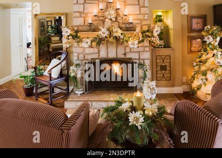 Two upholstered armchairs in front of natural cut stone wood burning fireplace with Christmas decorations in living room. Stock Photo