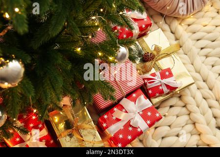 Pile of gift boxes near Christmas tree on white knitted blanket, above view Stock Photo