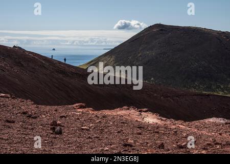 People walking on the volcanic slopes exploring the volcano, Eldfell, on the island of Heimaey, part of the Westman Islands, an archipelago of some... Stock Photo