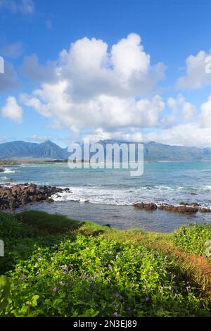View of the West Maui Mountains from the north shore of Maui with the turquoise waters of the Pacific Ocean and white puffy clouds in a blue sky Stock Photo