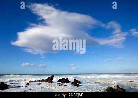 Rocks in surf and a dramatic cloud formation in a bright blue sky at Baldwin Beach; Paia, Maui, Hawaii, United States of America Stock Photo