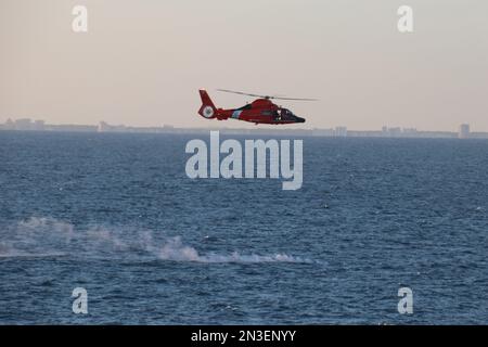 Myrtle Beach, United States of America. 04 February, 2023. A U.S Coast Guard MH-65 Dolphin helicopter hovers over the debris field of the Chinese high-altitude surveillance balloon as recovery operations begin on the Atlantic Ocean, February 4, 2023 off the coast of Myrtle Beach, South Carolina. The suspected spy balloon was shot down by American fighter aircraft on February 4th after traveling across the continental United States. Credit: Lt. Jerry Ireland/US Navy Photo/Alamy Live News Stock Photo