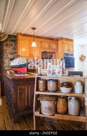 Glazed ceramic pots and jug on wooden shelves in kitchen with oak wood cabinets inside old 1835 fieldstone house. Stock Photo
