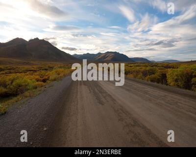 View of the Dempster Highway through the autumn landscape with the dramatic mountain peaks in the distance; Dawson City, Yukon, Canada Stock Photo