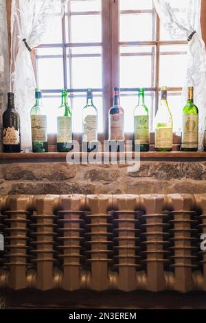 Empty wine bottles on windowsill and hot water heating radiator in dining room inside old 1835 fieldstone house. Stock Photo