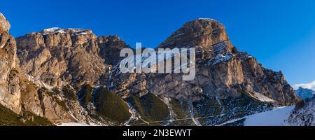 Rocky peaks of Sassongher Mountain covered in snow against a bright blue sky at Colfosco Corvara in Alta Badia Mountain Region; Dolomites, Italy Stock Photo