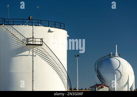 Large white spherical and round oil storage tanks with black metal stairs with shadows against a blue sky, North of Longview, Alberta; Alberta, Canada Stock Photo