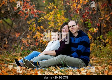 A mother and father spending some qualtiy time together with their son and looking at the camera during a family outing in a city park during the f... Stock Photo