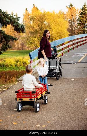 A mother and her young children crossing a bridge over a river in a city park during the fall season and her baby daughter has Down Syndrome Stock Photo